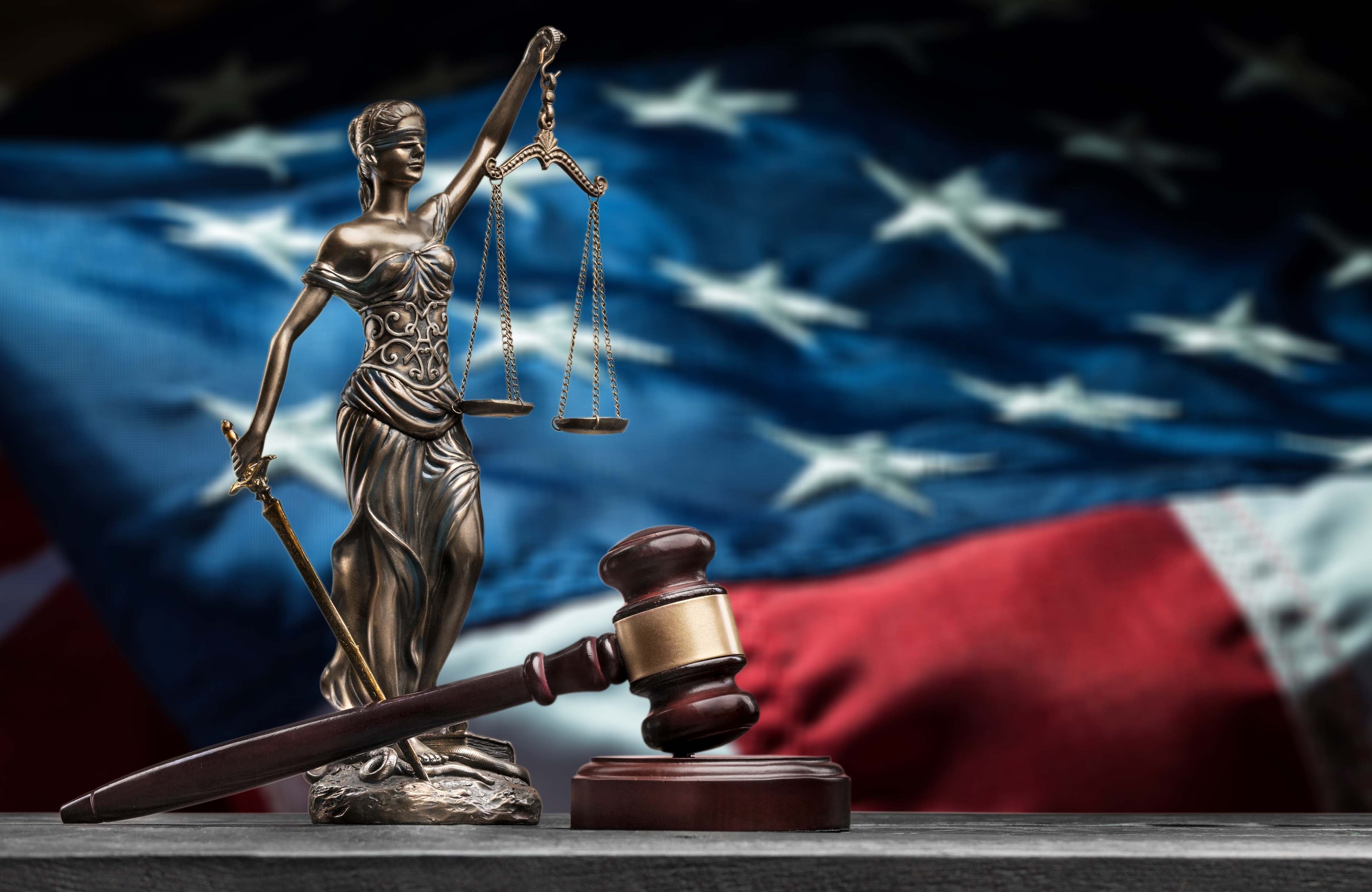 Closeup of a sculpture of Themis, the scales of justice, before an American flag